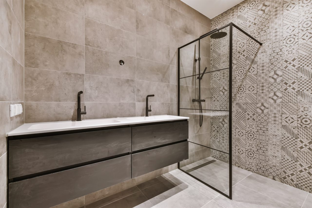 Moderne badkamer met donker dubbel badkamermeubel, inloopdouche met zwarte glazen wand en lijnafvoer, patroontegels op de douchewand en een matte grijze tegelvloer