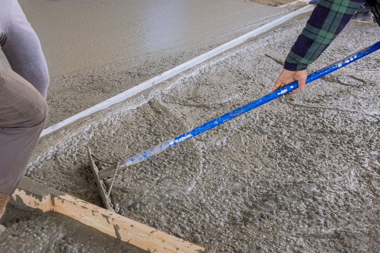 Twee vakmensen trekken verse chape vlak met een blauwe rijlat, met houten bekisting op de voorgrond