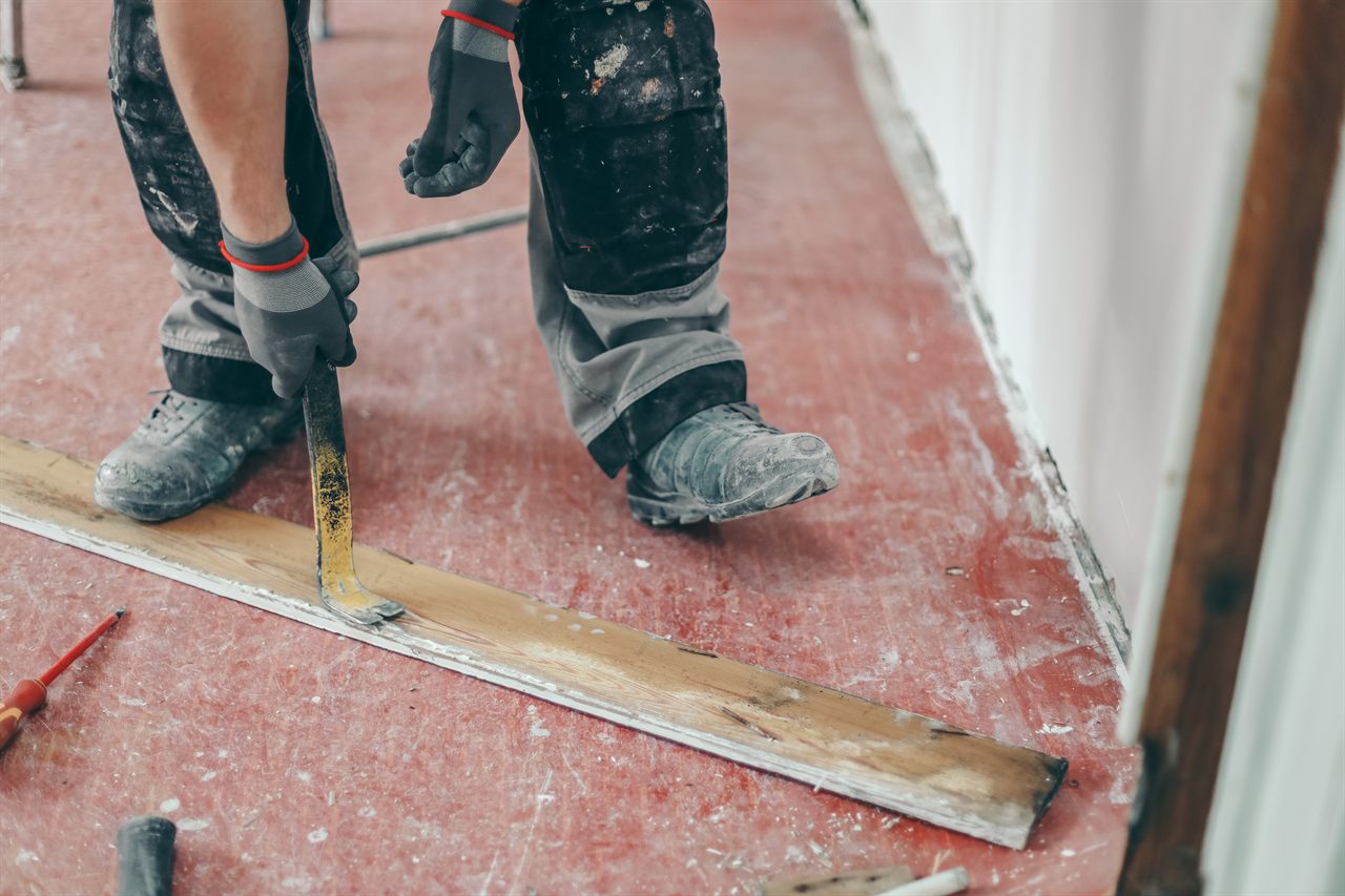Vakman wrikt met een koevoet een oude houten plint los tijdens de uitbraak van een vloer